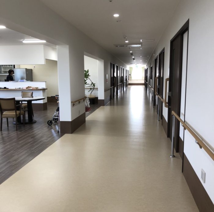 介護施設の廊下。受付カウンターと複数の居室ドアが見える。