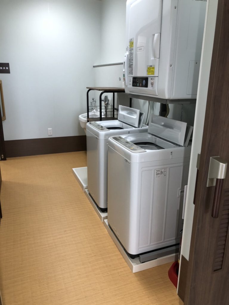 介護施設の共用洗濯室。複数の全自動洗濯機と乾燥機が設置されている。